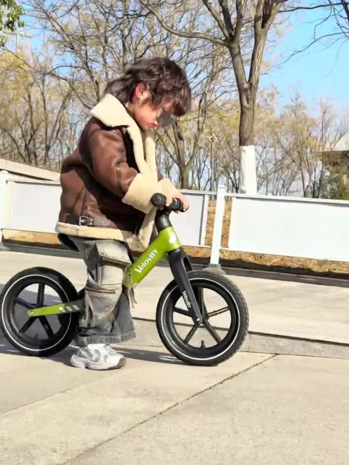 Copil pe bicicletă fără pedale Velovity verde, în parc