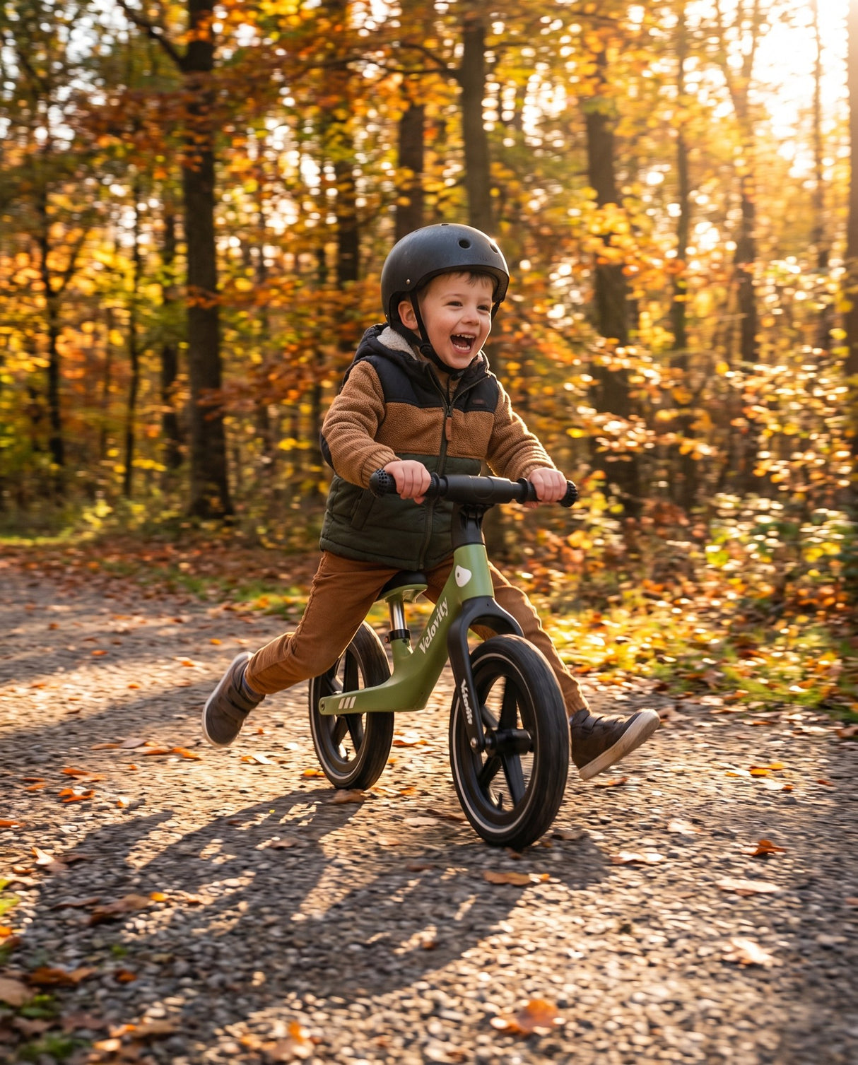 Băiețel cu cască alunecă pe bicicleta fără pedale verde matcha cu roți gonflabile, pe potecă de pădure