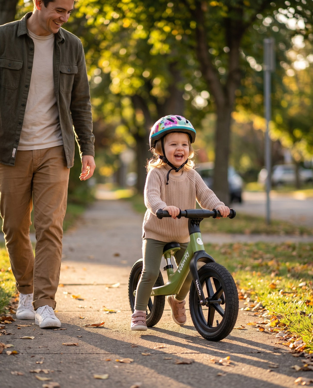 Fetiță cu cască pe bicicleta fără pedale verde matcha cu roți gonflabile, alături de părinte