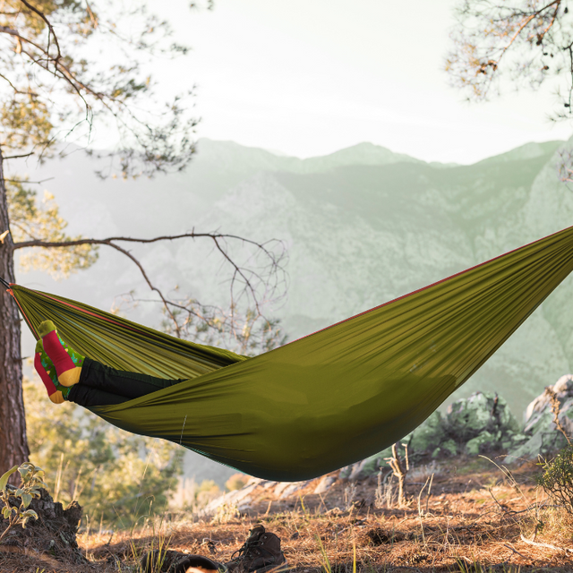 Hamac hikerjoy PRO green army montat între copaci, cu muntți în fundal