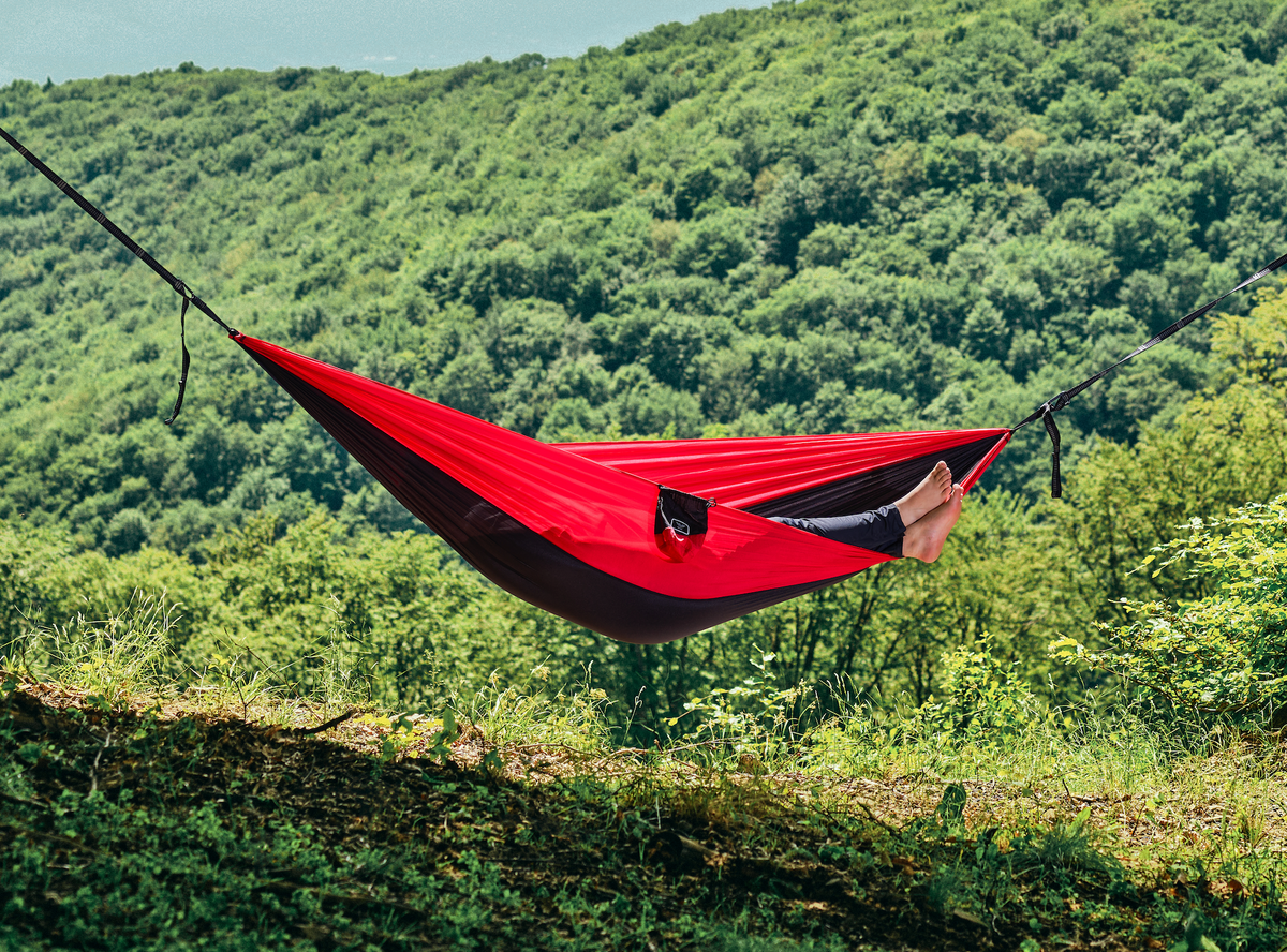 Persoană relaxându-se în hamacul hikerjoy roșu cu negru în natură