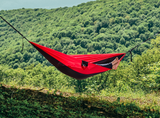 Persoană relaxându-se în hamacul hikerjoy roșu cu negru în natură