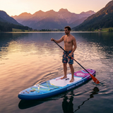 Bărbat pe placa SUP Aurora Borealis albastru-mov, pe lac montan la apus