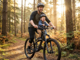 Tată și copil pe bicicletă MTB cu scaun frontal pentru copii montat pe cadru, pe traseu forestier
