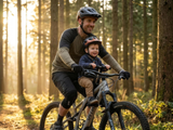 Plimbare cu copilul în scaunul frontal de bicicletă pe potecă de pădure la apus