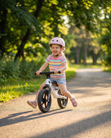 Fetiță cu cască se plimbă cu bicicleta fără pedale alb perlat Velovity în parc